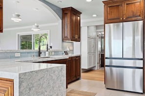 A modern kitchen with marble countertops, wooden cabinets, stainless steel appliances, and pendant lighting. - Serene Mountain Home with Ocean View! (Aptos)