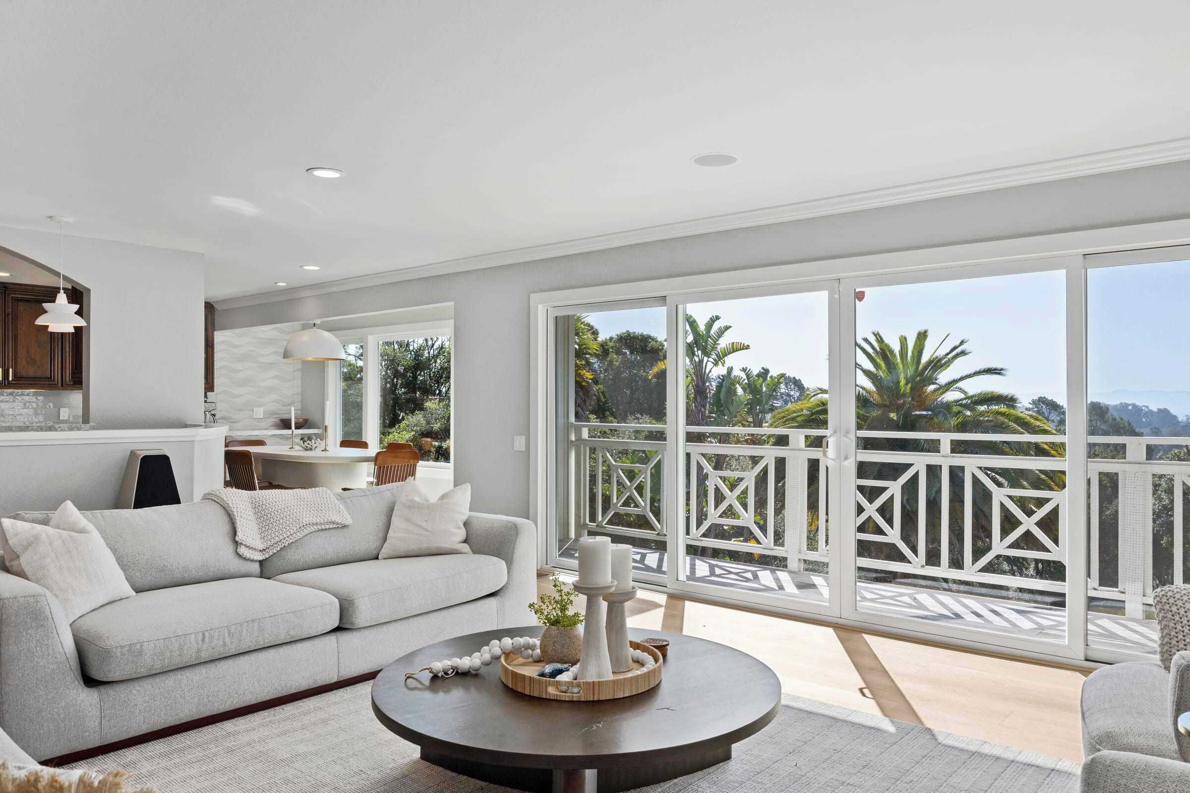 A spacious living area with a sofa, a round coffee table, and a view of a balcony with a railing.