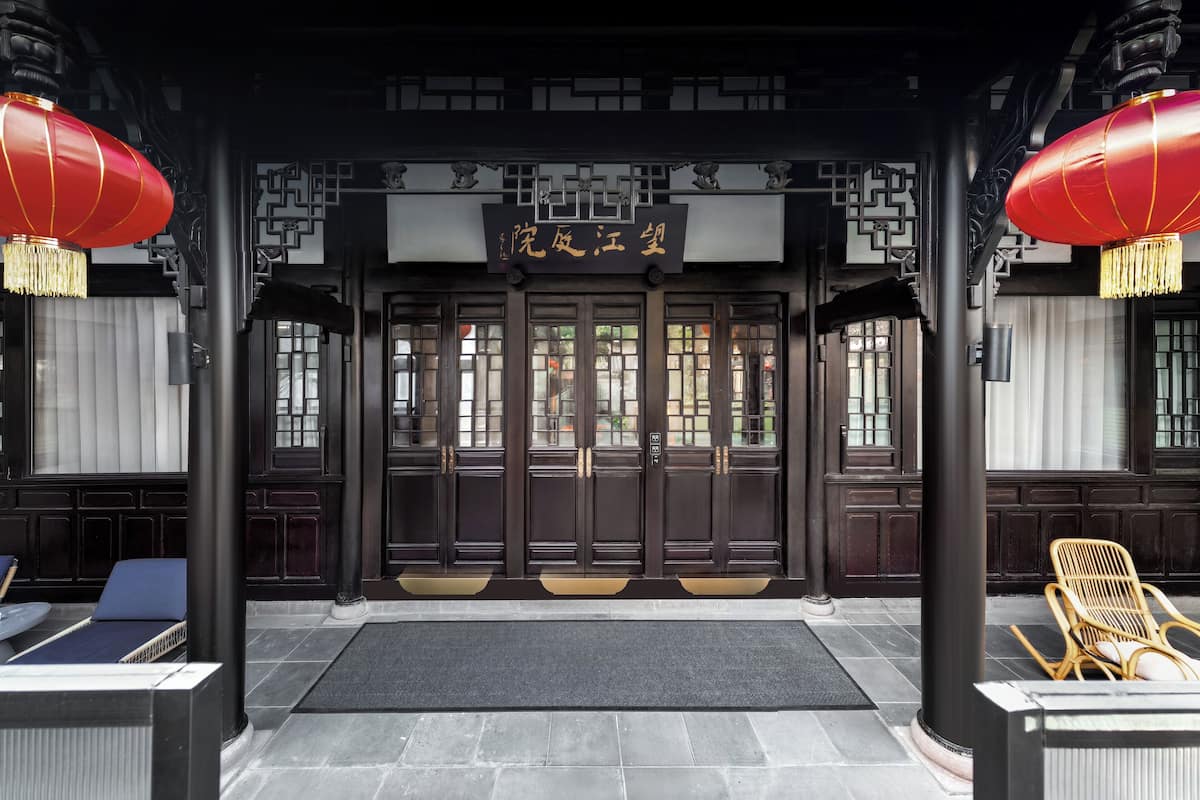 A traditional Chinese building entrance with dark wooden doors, a sign with Chinese characters, and two red lanterns.