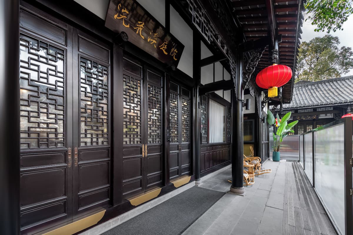 A traditional building with dark wooden doors, a sign with Chinese characters, and a red lantern.