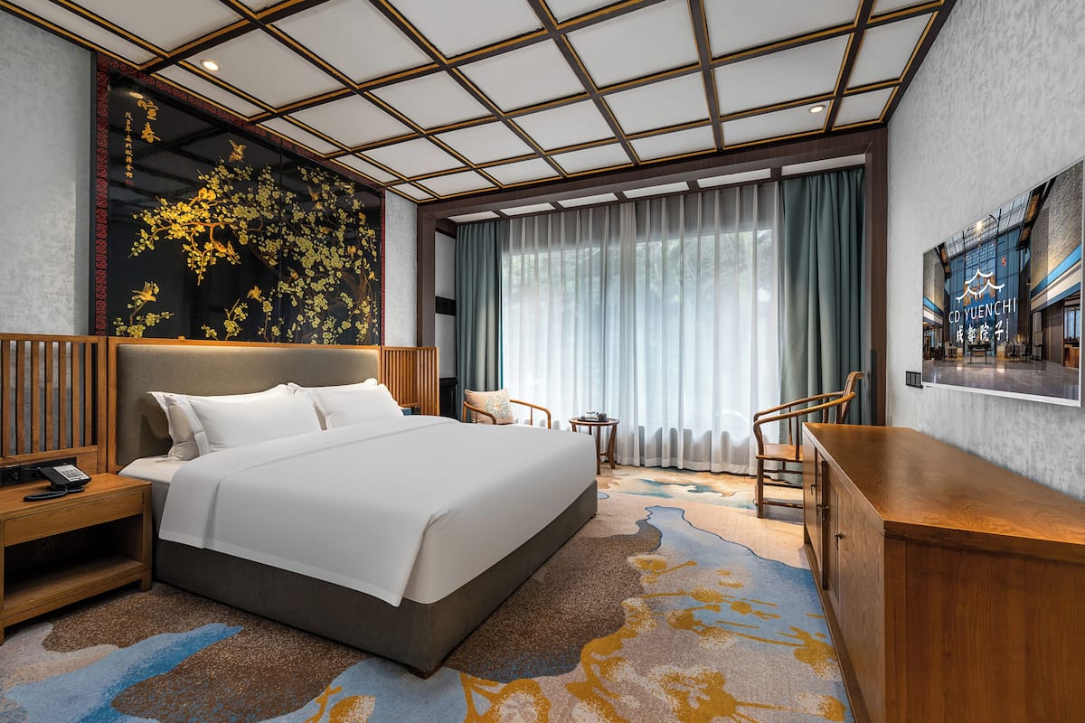 A modern hotel room with a large bed, a desk, and a view of the city.