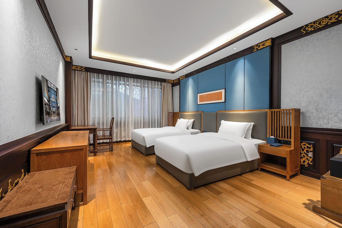 A hotel room with two beds, a desk, and a chair.