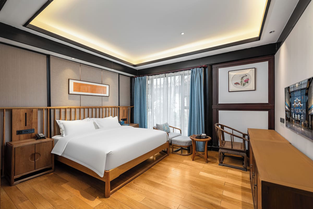 A modern hotel room with a large bed, wooden nightstands, a small table, and a desk.