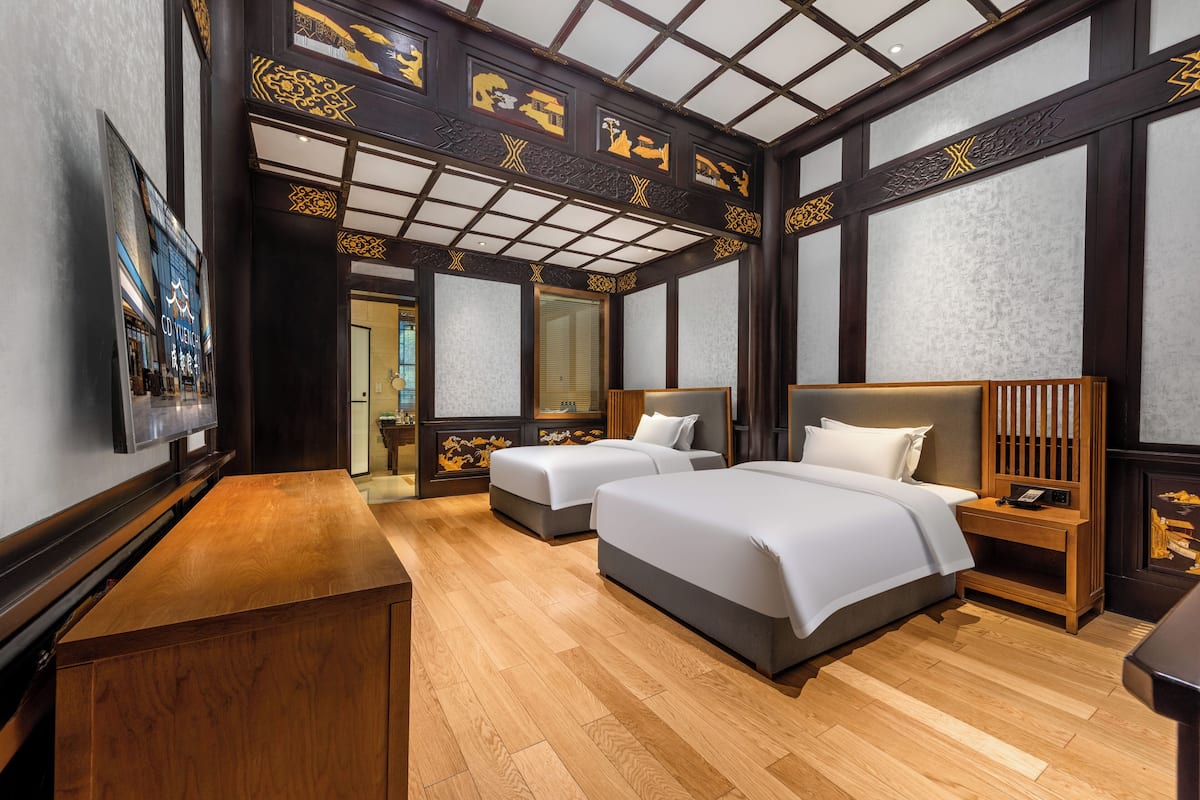 A hotel room with two beds, a wooden desk, a television, and a large mirror.