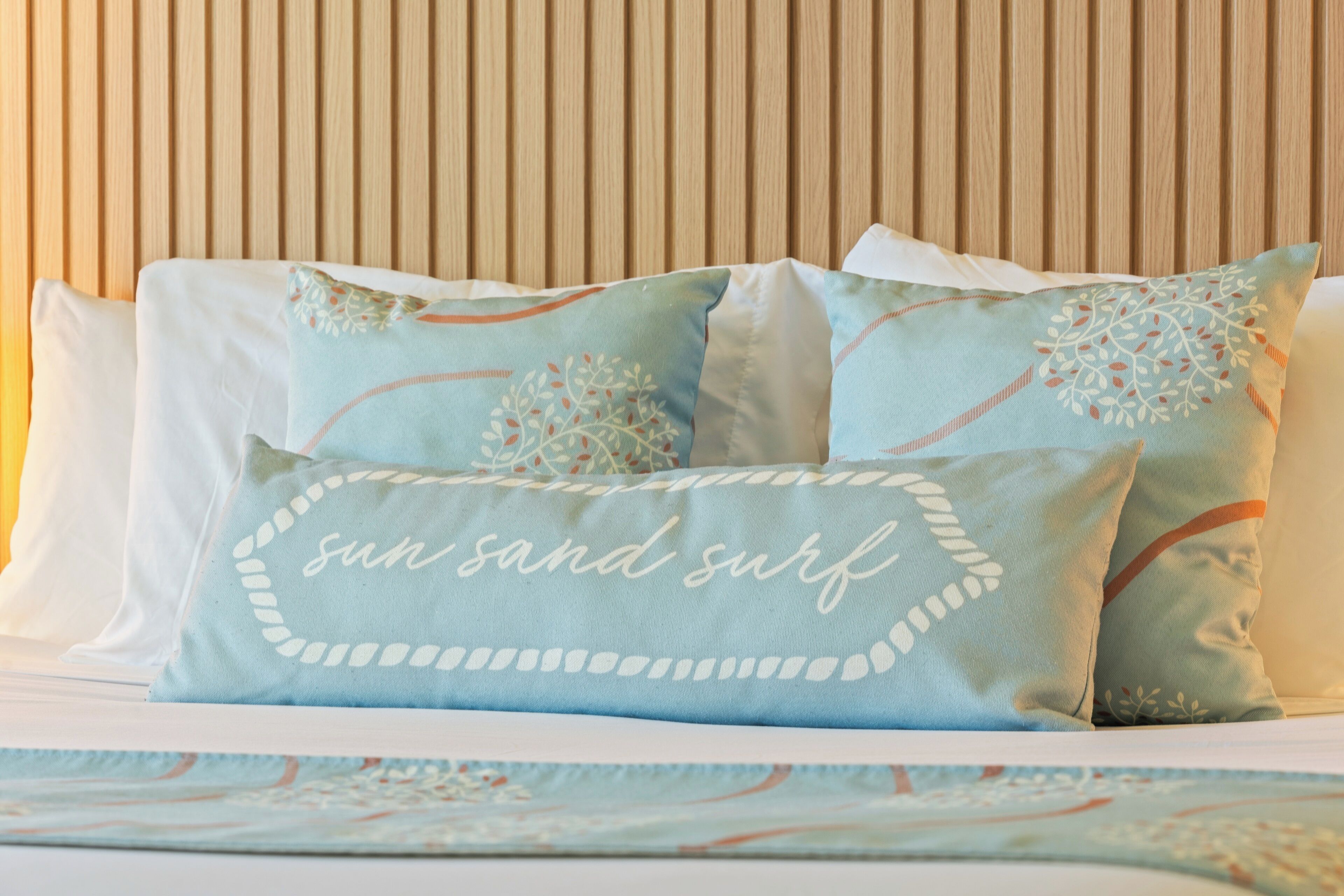 Een bed met kussens in een strandthema, waaronder een kussen met de tekst 'sun sand surf'.