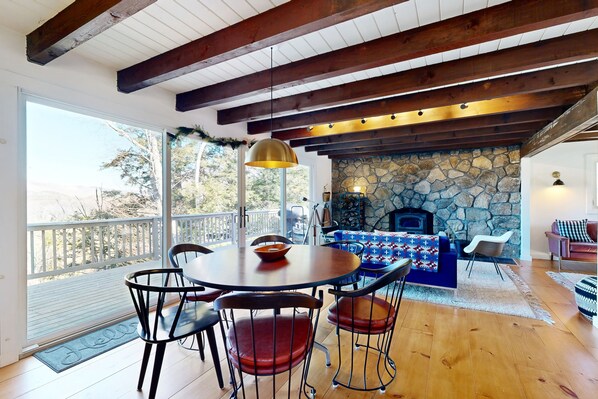 Cozy living area with a fireplace, wooden ceiling, and large window offering a view of the outdoors.