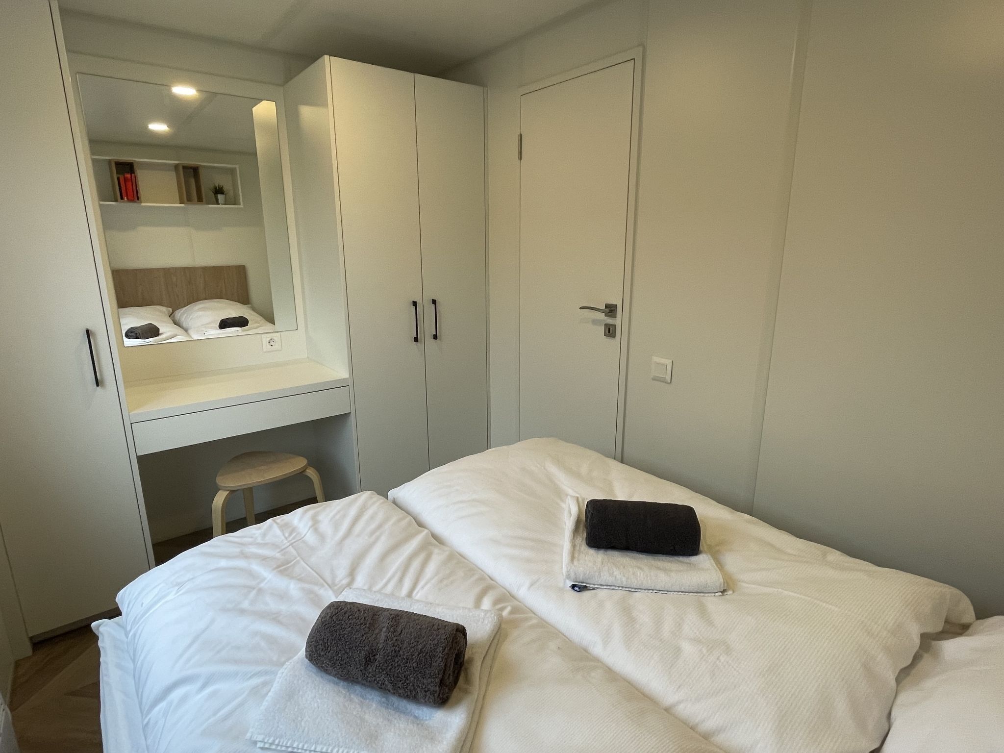 Un dormitorio con cama, dos toallas, un taburete pequeño y un armario.