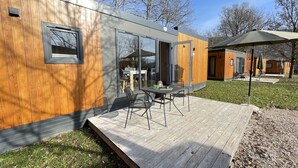 Une maison moderne en bois, dotée d’une terrasse, de grandes fenêtres et d’un coin repas.