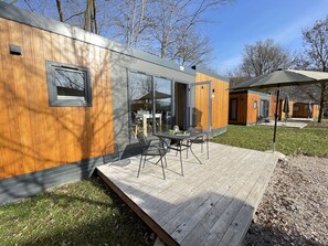A modern wooden house with a deck, large windows, and a dining area.