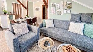 Una sala de estar moderna con un sofá gris, un comedor con mesa de madera y una cocina visible al fondo.