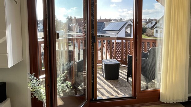 Habitación con puerta de cristal corredera que da a una terraza exterior con vista a casas vecinas y un panel solar.