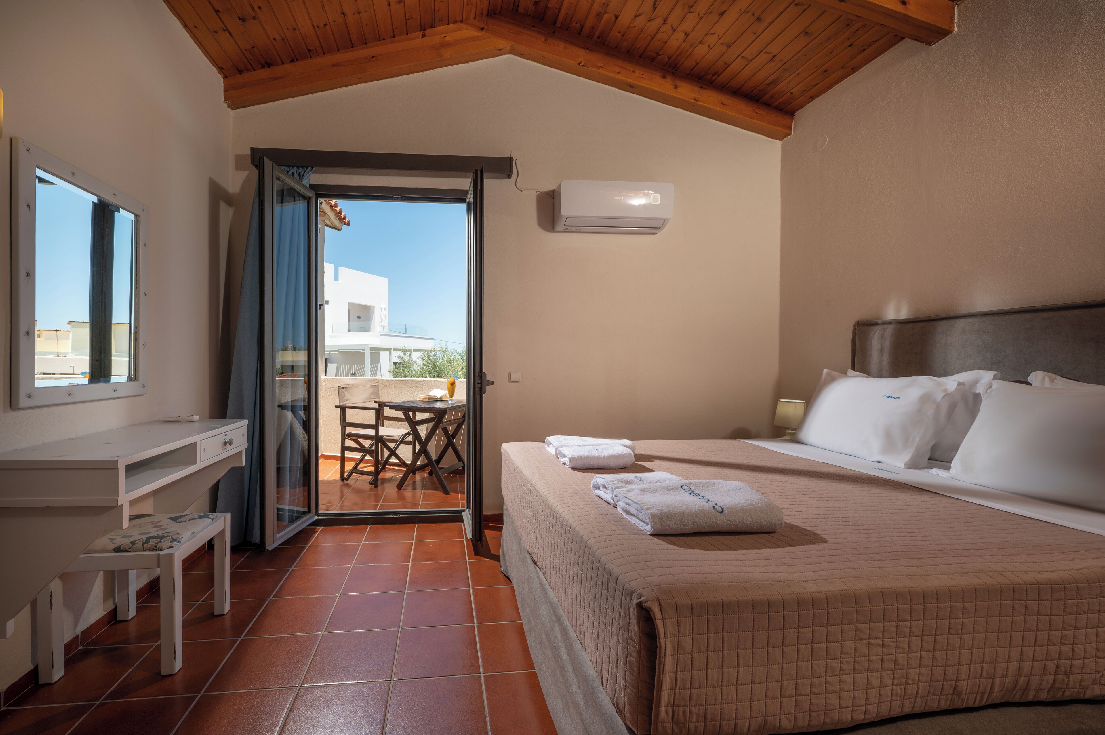 A bedroom with a bed, a desk, and a chair. There is a window and an air conditioning unit on the wall.