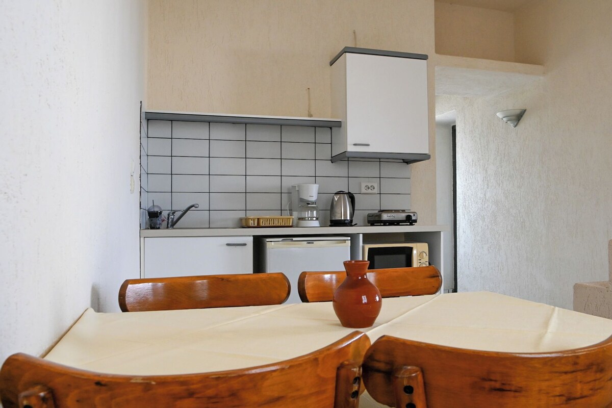 A kitchen with a white cabinet, a microwave, and a toaster on the countertop. There is a wooden table with a white tablecloth and two chairs.