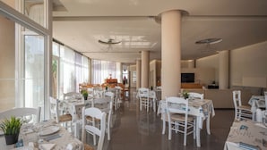 A spacious dining area with white tables and chairs, large windows, and a modern ceiling design. - Creteco Hotel & Suites (Hersonissos)