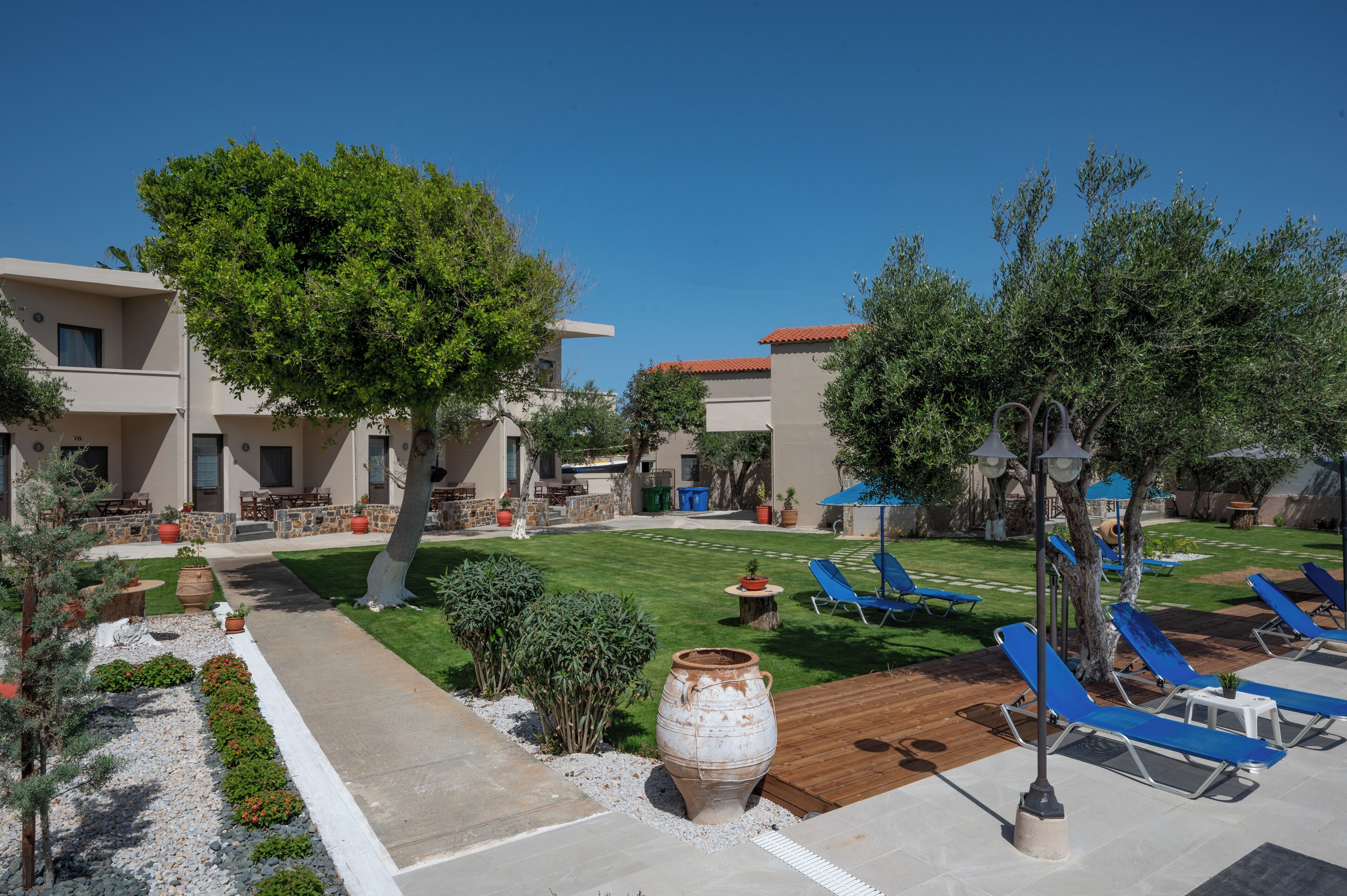 Un patio con mobiliario exterior, una maceta grande y una zona de piscina con sillones de descanso.
