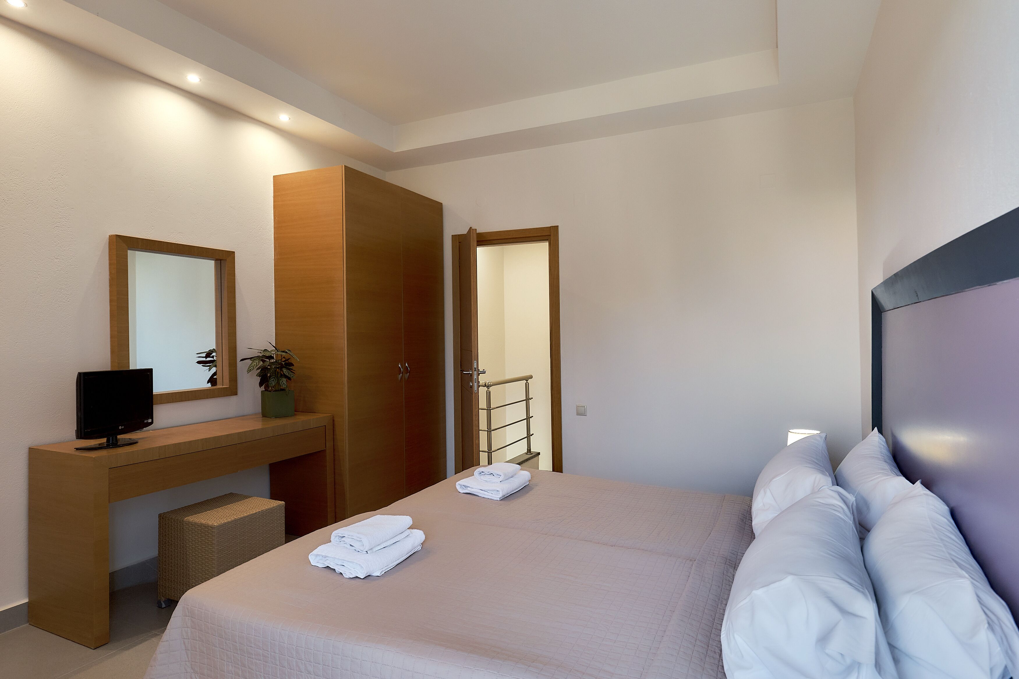 A hotel room with a bed, a desk with a computer, a mirror, and a wardrobe.