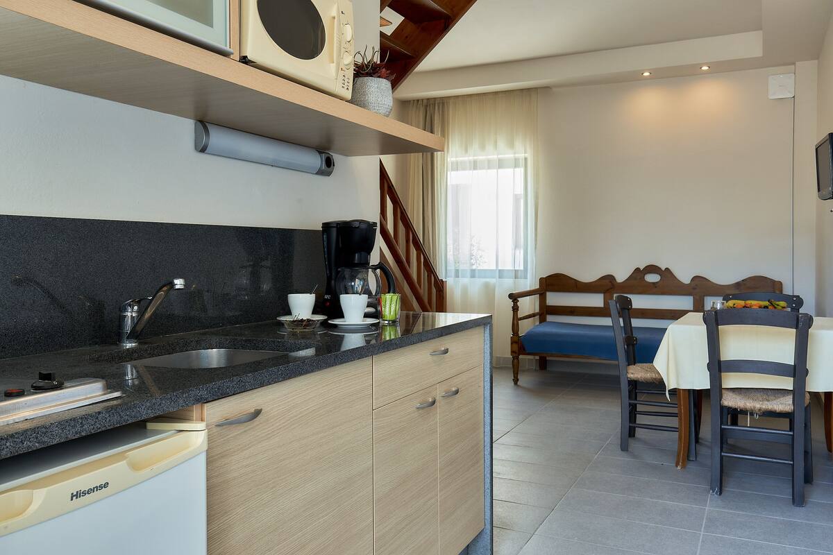 A modern kitchen with a Hisense dishwasher, a black countertop, and a wooden dining area with a bench and chairs.