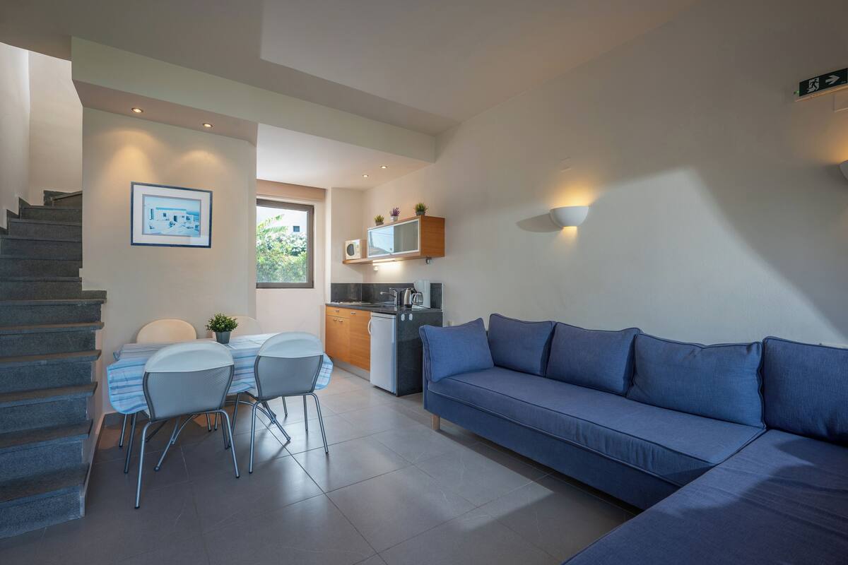 A modern living room with a sofa, dining table, chairs, and a kitchen area with a microwave and sink.