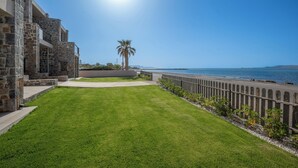 A well-maintained lawn with a stone building, a palm tree, and a beach view. - Creteco Hotel & Suites (Hersonissos)