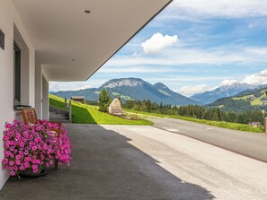 Un porche de hotel con vistas a montañas, una construcción de piedra y un parterre de flores.