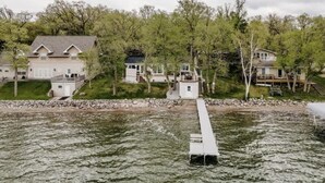 A lakeside property with a dock extending into the water, surrounded by multiple houses with a grassy area and trees. - Sunset Beach View on Otter Tail Lake (Otter Tail)