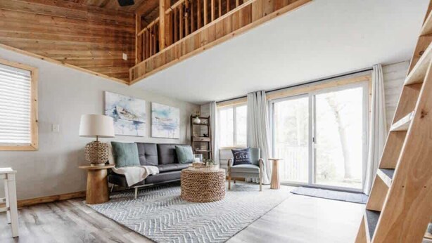 A spacious living room with a high ceiling, a sofa set, a coffee table, and a large window. - Sunset Beach View on Otter Tail Lake (Otter Tail)