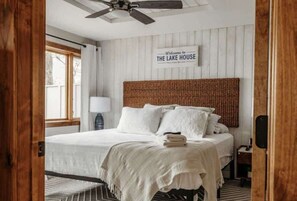 A bedroom with a bed, a ceiling fan, a sign reading 'Welcome to The Lake House,' and a window with curtains. - Sunset Beach View on Otter Tail Lake (Otter Tail)