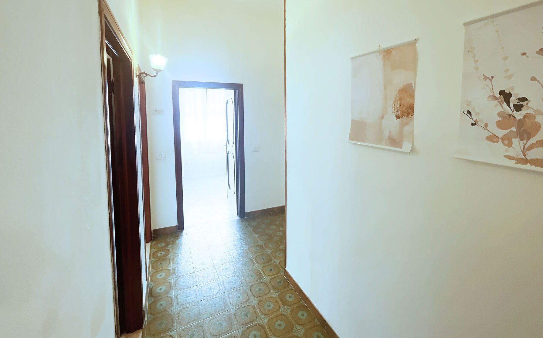 A hallway with patterned floor tiles, a door leading to another room, and two wall-mounted artworks.