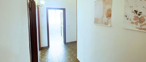 A hallway with patterned floor tiles, a door leading to another room, and two wall-mounted artworks.