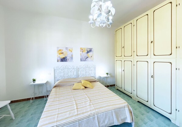 A bedroom with a bed, two bedside tables, a chandelier, a wardrobe, and two wall-mounted paintings.