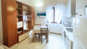 A kitchen with a dining table, chairs, a wooden cabinet, and a window with curtains. - Casa Diana, a few steps from Porto Azzurro center! (Porto Azzurro)