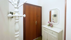 A hallway with a wooden door, a white wall-mounted telephone, and a white console with a mirror and a vase of flowers. - Casa Diana, a few steps from Porto Azzurro center! (Porto Azzurro)