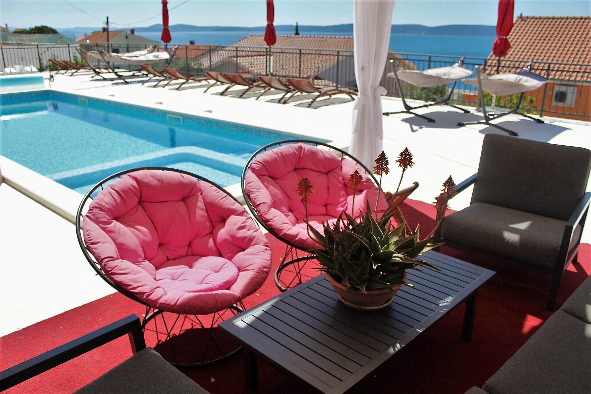 A poolside area with lounge chairs, a table, and a potted plant.