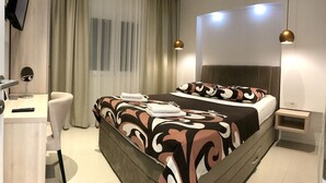 Camera d'albergo moderna con un letto grande, una scrivania con sedia, una TV e un comodino.