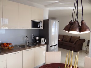 A modern kitchen with a microwave, refrigerator, and coffee maker. There is a dining area with a table and chairs, and a sofa in the background.