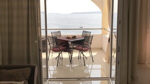 Un balcone con tavolo e sedie, vista sul mare e una porta in vetro.