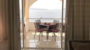 Un balcón con mesa y sillas, vista al mar y un velero en la distancia.