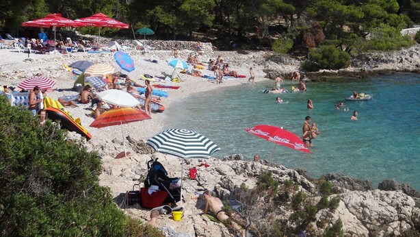 Una playa con gente tomando el sol, nadando y usando sombrillas.