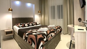 Una habitación de hotel moderna con una cama grande, mesitas de noche, un escritorio y un televisor.