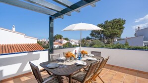 Une terrasse avec une table dressée pour le repas, entourée de chaises, et un parasol pour faire de l’ombre.