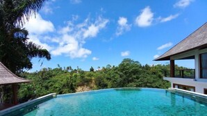 A clear blue infinity pool with a view of lush greenery and a wooden structure.