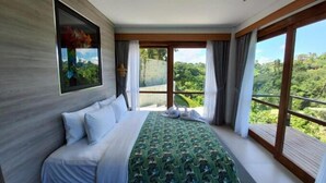 A bedroom with a large bed, a view of greenery, and a painting on the wall.