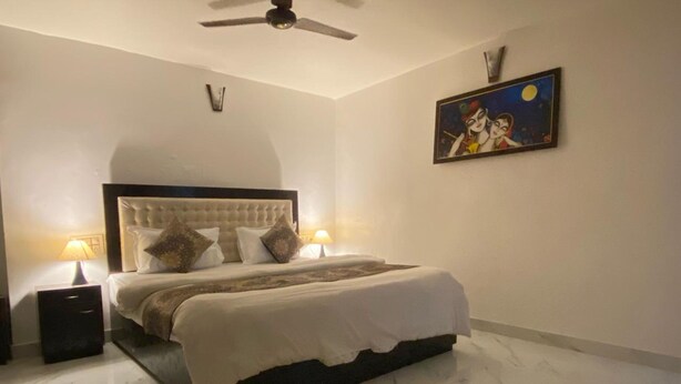 A bedroom with a large bed, two bedside tables, a ceiling fan, and a painting on the wall.