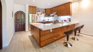 A modern kitchen with wooden cabinets, a large island with bar stools, stainless steel appliances, and a hanging pot rack.