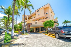 A multi-story hotel with a prominent entrance, palm trees, and a paved driveway.