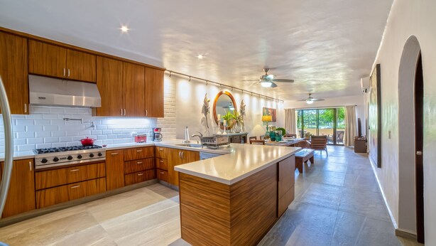 A modern kitchen with wooden cabinets, a central island, and a large window providing natural light.