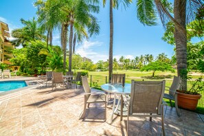 A poolside area with a table and chairs, surrounded by palm trees and a view of a golf course.