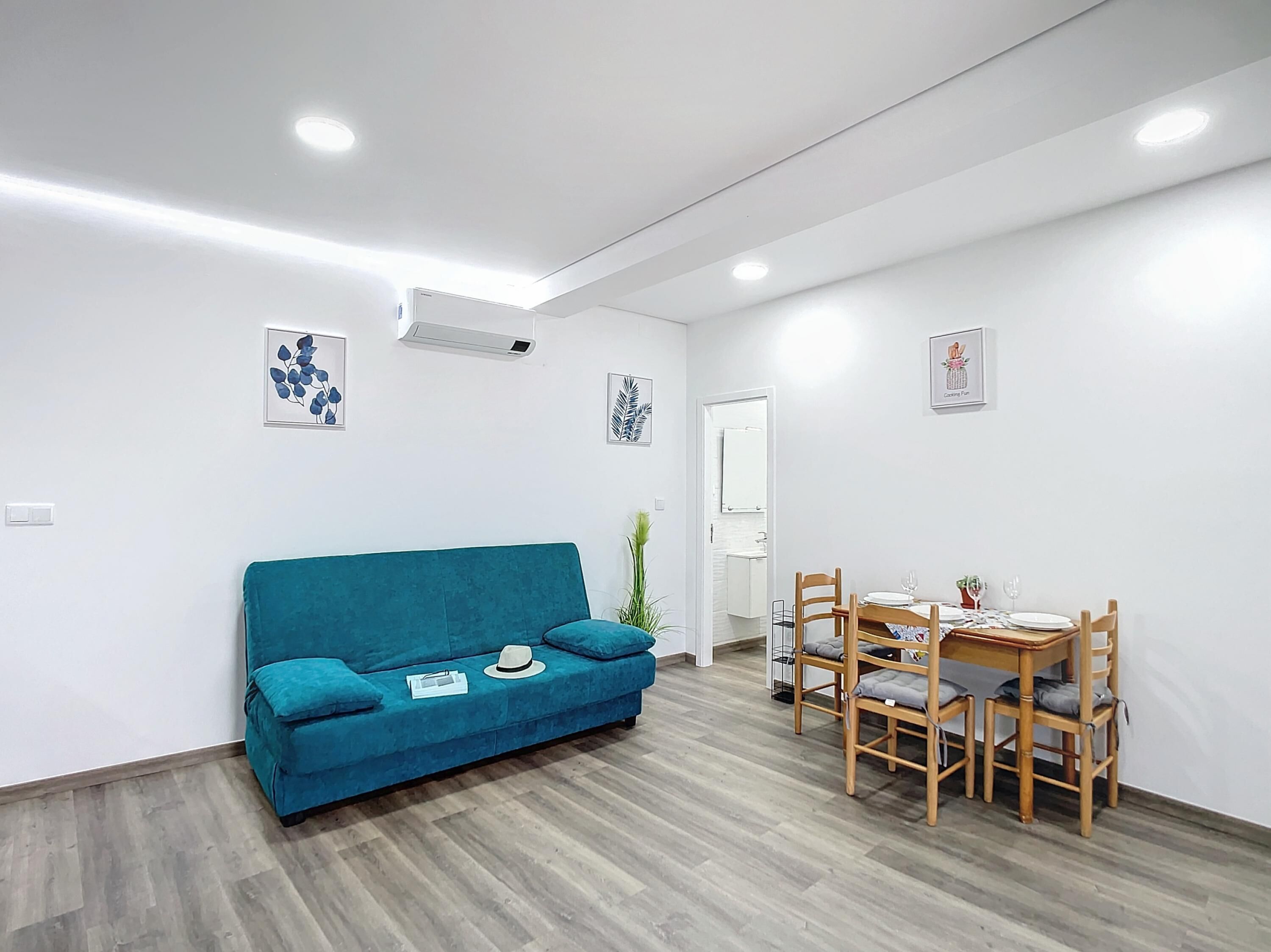 Een moderne woonkamer met een blauwgroene bank, een eettafel met stoelen en een kleine plant.