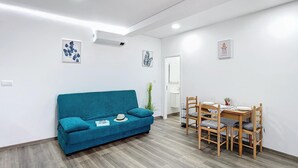 A modern living room with a teal sofa, a dining table with chairs, and a small plant. - Gomes House by Atlantic Holiday (Ponta do Sol)