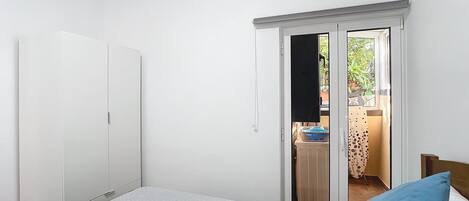 A bedroom with a bed, a wardrobe, and a sliding door leading to a balcony with a sink and potted plants.